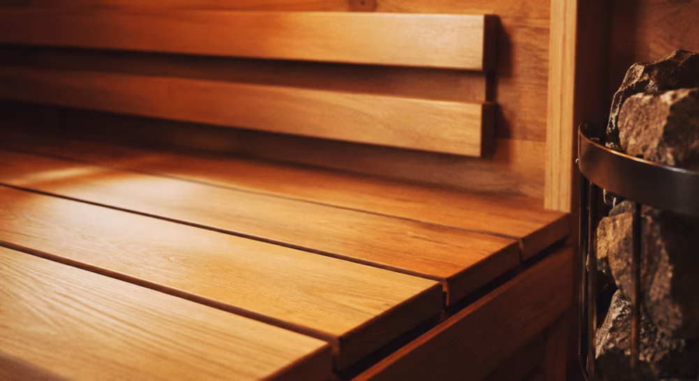Close-up of a sauna interior in warm thermo-treated spruce, smooth bench wood and natural stone heater visible.
